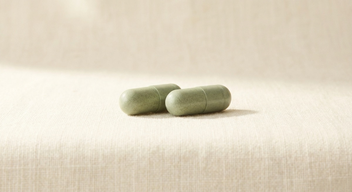 Macro of two sage-green capsules on warm linen